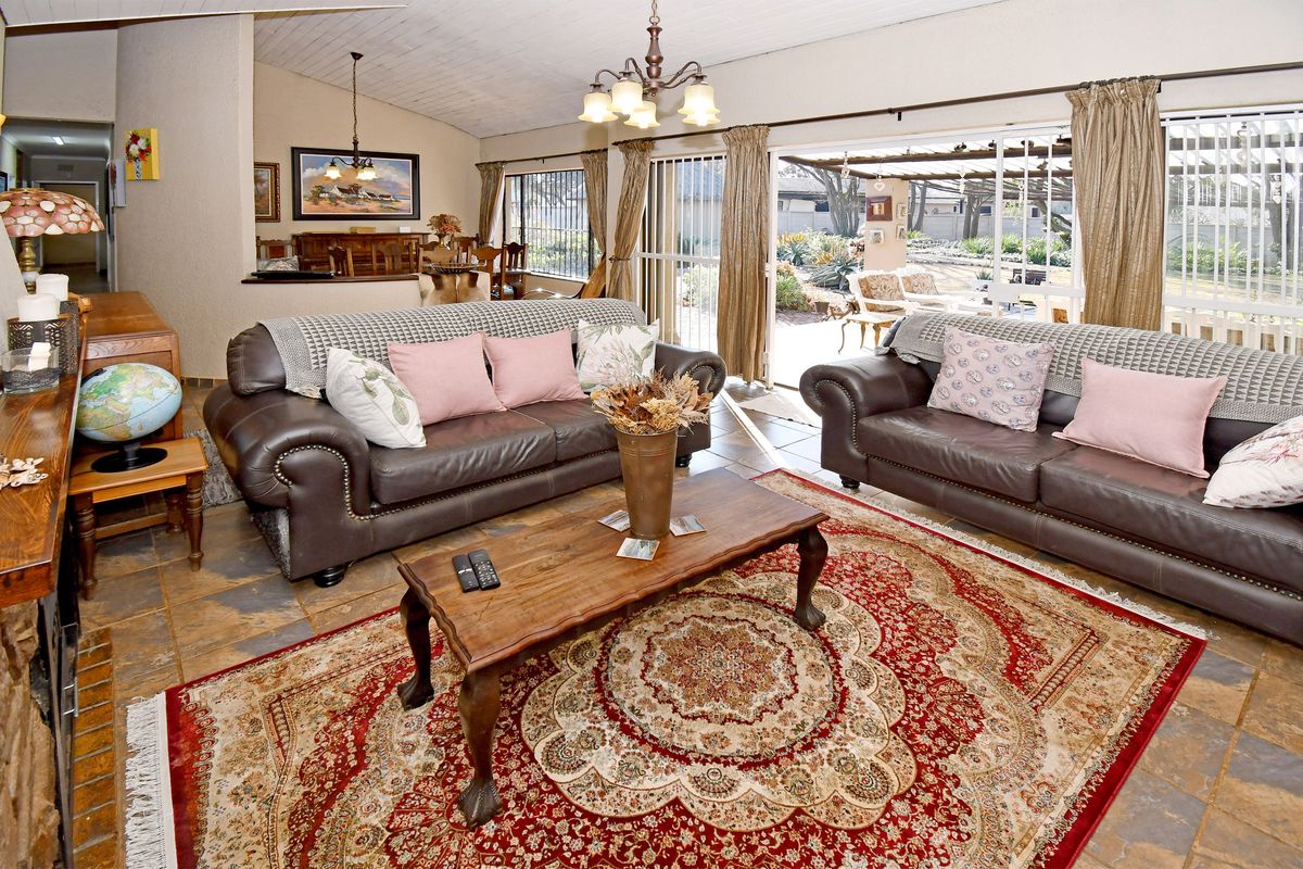 Spacious living room featuring stone tile flooring, vaulted ceilings with exposed beams, and large sliding glass doors providing direct access to the outdoor patio area.