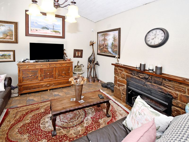 Cozy living room featuring a rustic stone fireplace, tiled flooring, and a timber ceiling, creating a warm and traditional atmosphere.