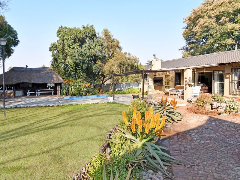 Spacious rear garden featuring a swimming pool, a traditional thatched lapa, and a covered patio area with a built-in braai.