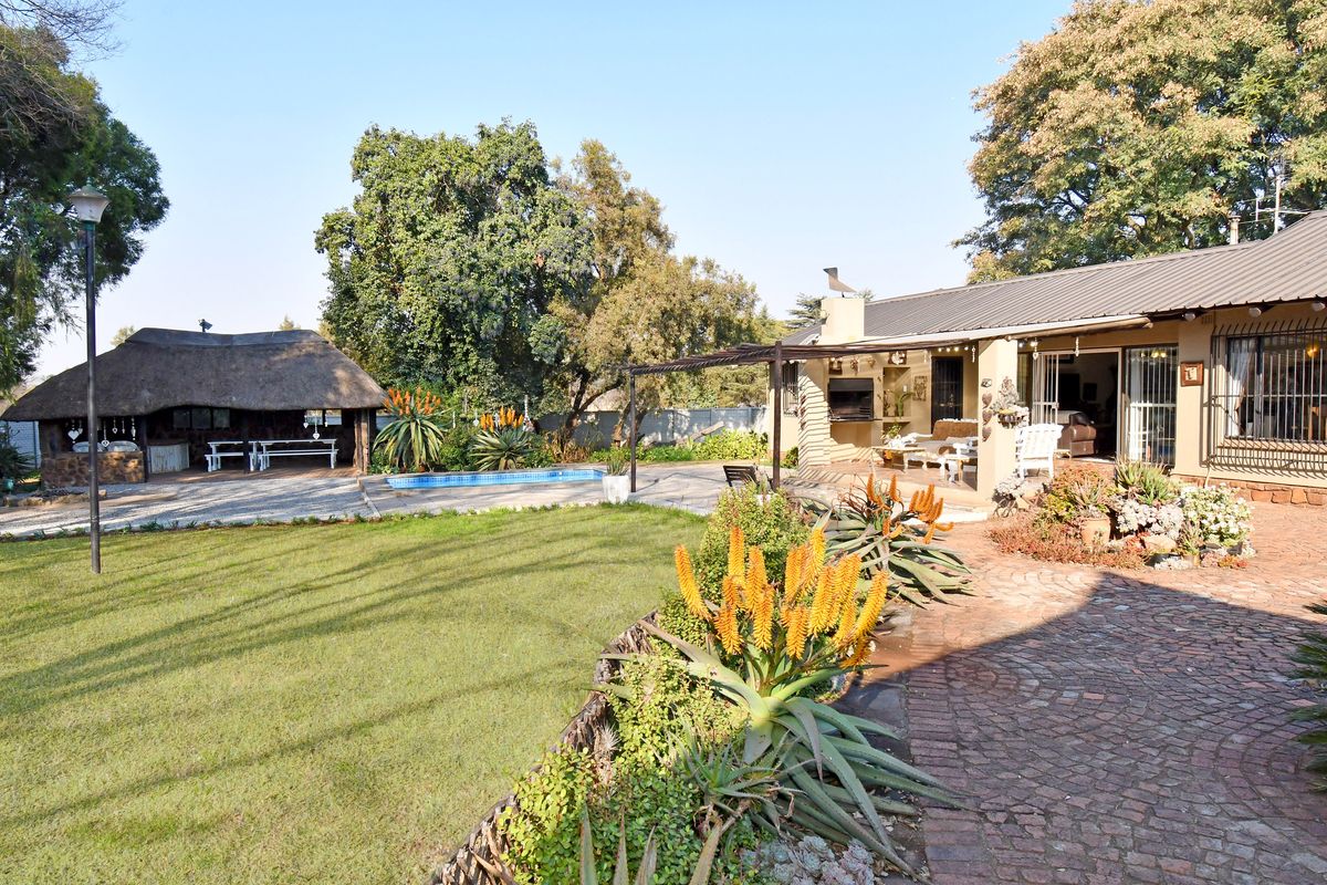 Spacious rear garden featuring a swimming pool, a traditional thatched lapa, and a covered patio area with a built-in braai.