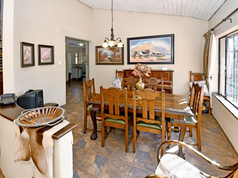 A dining room featuring tiled flooring, exposed beam ceilings, and large windows with security bars, providing a functional space for family meals.