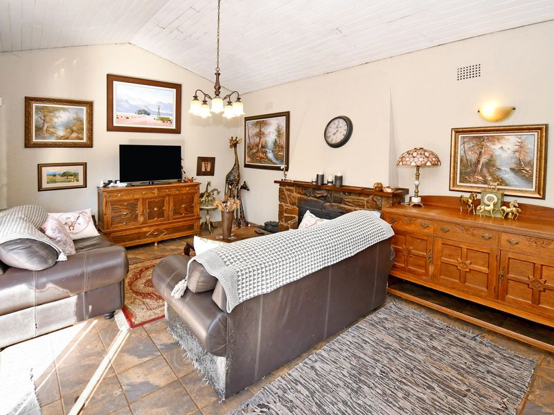 A cozy living room featuring a stone fireplace, vaulted timber ceiling, and tiled flooring, offering a warm and traditional atmosphere.