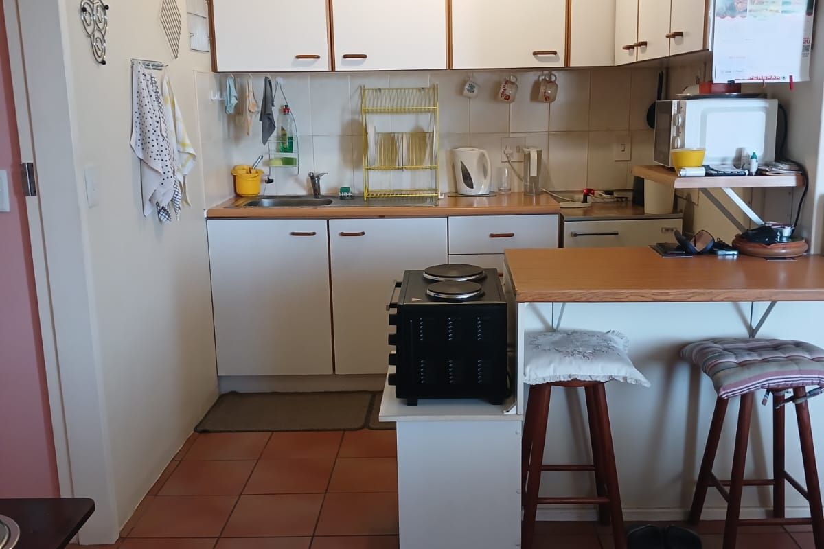 A compact kitchen featuring white cabinetry, laminate countertops, a breakfast bar, and tiled flooring, offering a functional layout with potential for modern updates.