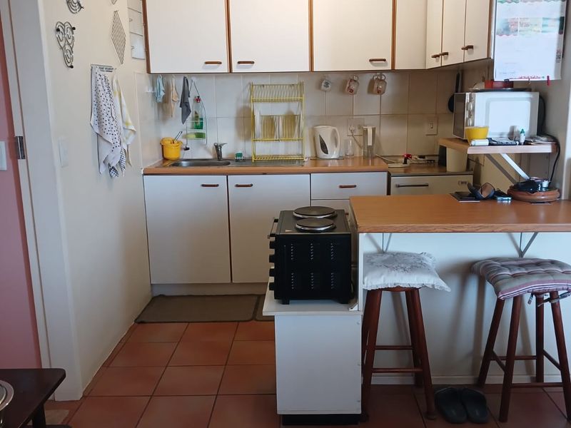 A compact kitchen featuring white cabinetry, laminate countertops, a breakfast bar, and tiled flooring, offering a functional layout with potential for modern updates.