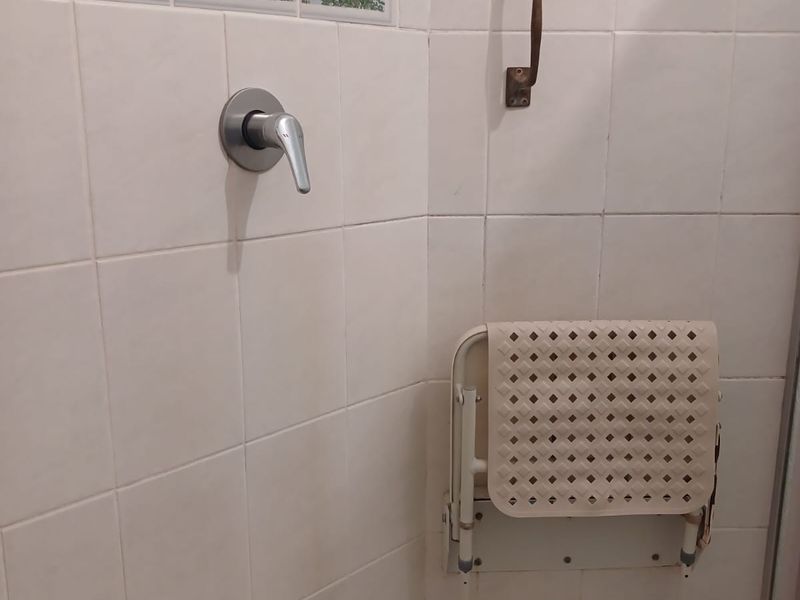 A shower enclosure featuring white wall tiles with decorative accents, a chrome mixer tap, and a wall-mounted grab rail.