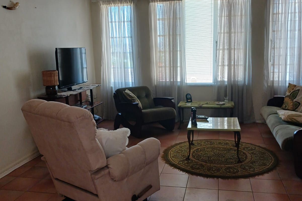 A living room featuring terracotta floor tiles, a ceiling fan, and large windows that provide ample natural light.
