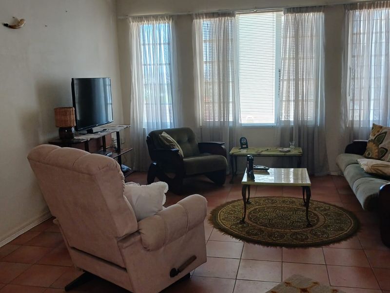 A living room featuring terracotta floor tiles, a ceiling fan, and large windows that provide ample natural light.