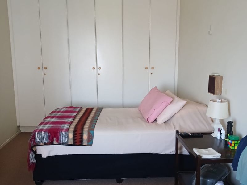 A bedroom featuring wall-to-wall built-in cupboards, carpeted flooring, and a wall-mounted air conditioning unit.