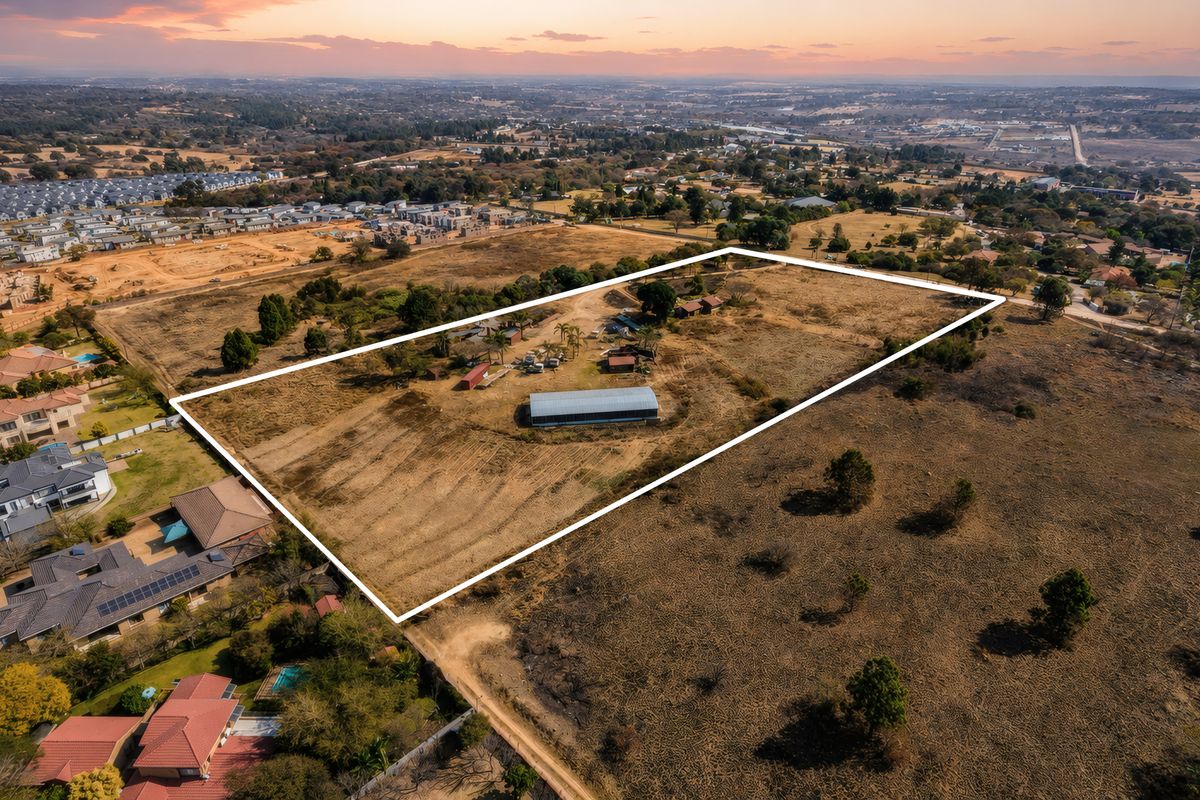 Aerial view of a large, vacant residential land plot featuring a metal shed structure and expansive open space in a developing suburban area.