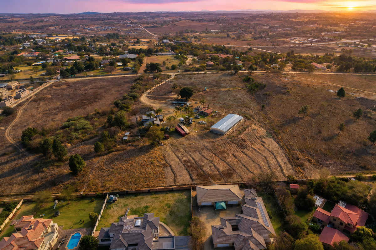 Aerial view of a large residential vacant land plot featuring existing outbuildings, a large shed, and surrounding rural landscape at sunset.