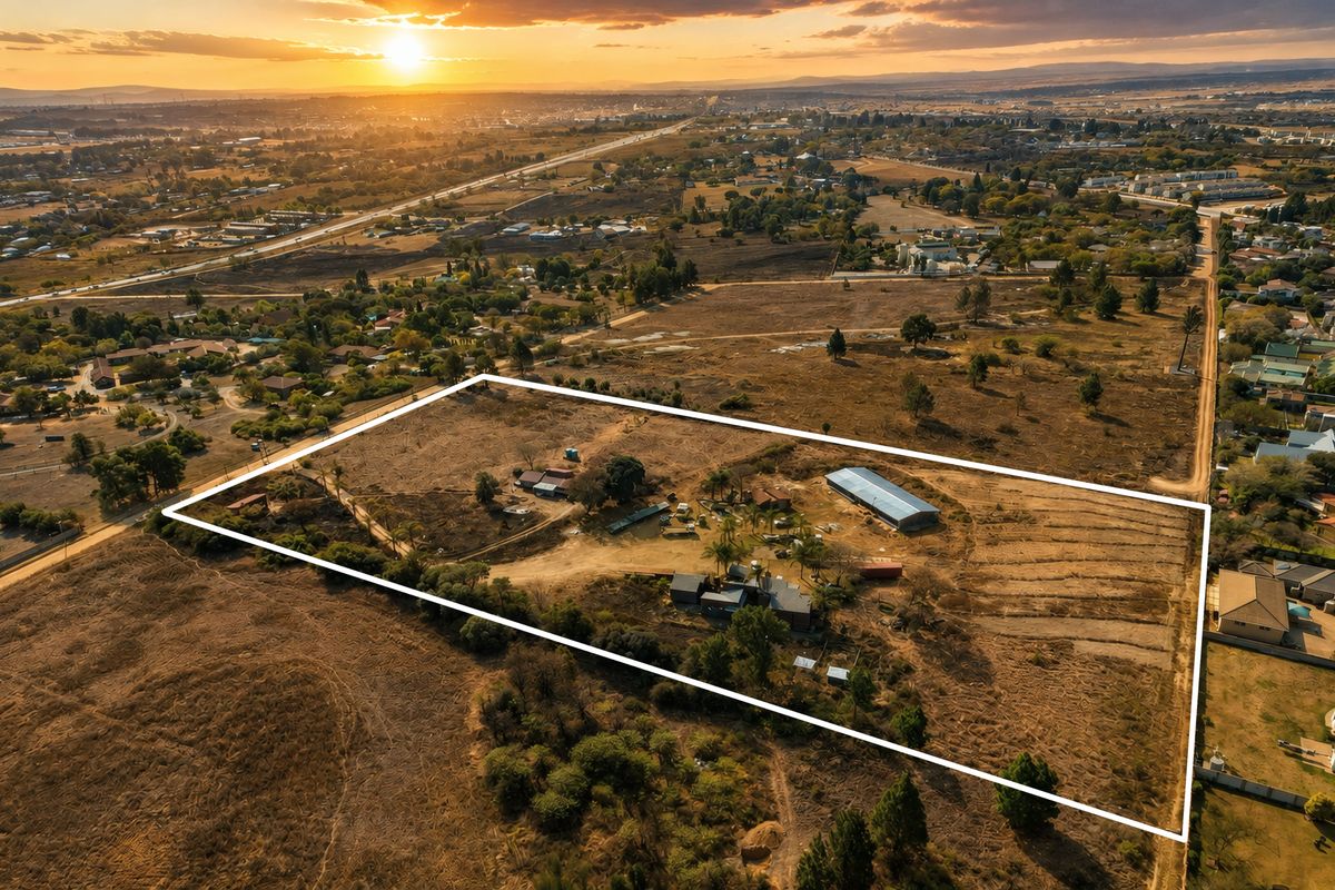 Aerial view of a large residential vacant land plot featuring existing outbuildings, a large shed, and established trees at sunset.