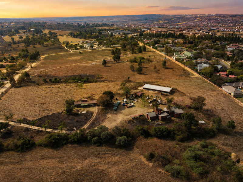 An aerial view of a large residential vacant land plot featuring existing outbuildings, perimeter fencing, and surrounding rural landscape.
