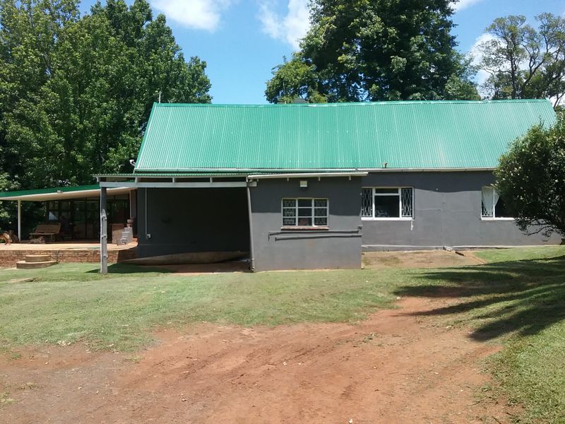 Rear view of a farm-style dwelling featuring a green corrugated metal roof, grey painted exterior walls, and an attached covered patio area.