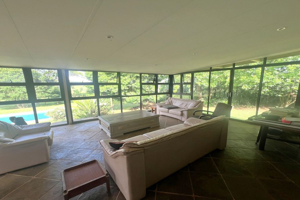 Spacious sunroom featuring extensive floor-to-ceiling windows, natural stone flooring, and direct views of the garden and pool area.