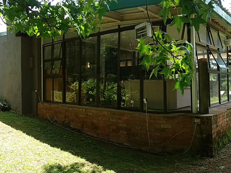 A rear view of the farm property featuring an enclosed sunroom with large glass windows and a brick base, set within a garden.