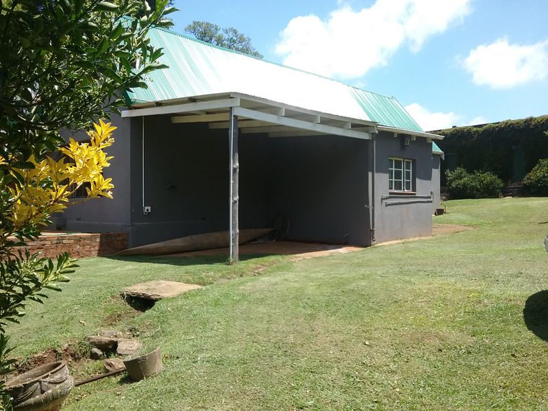 A view of the rear exterior of the farm building, featuring a covered patio area, green metal roof, and surrounding lawn.