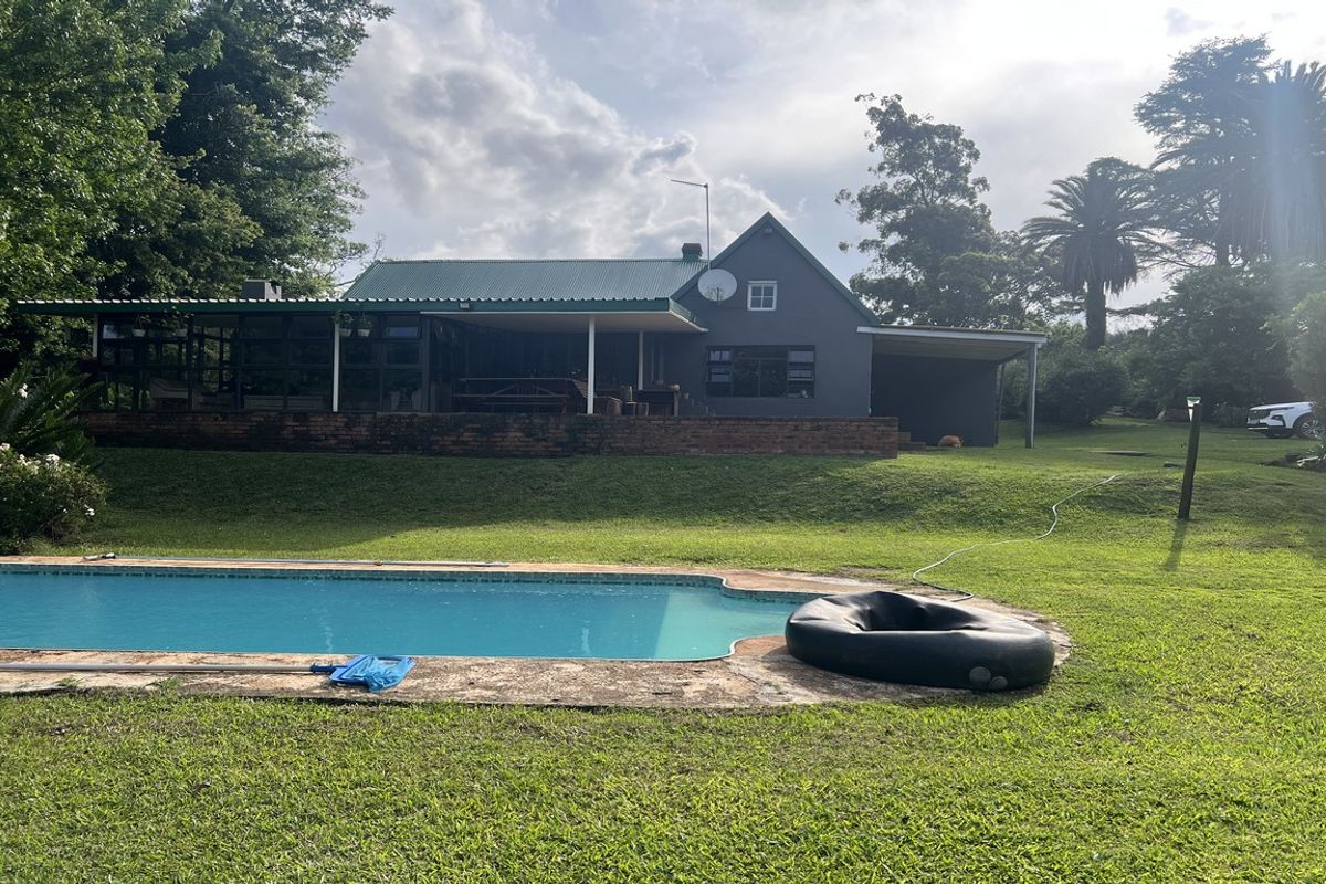 Rear view of the farmhouse featuring a swimming pool, expansive lawn, and a covered patio area with a metal roof.