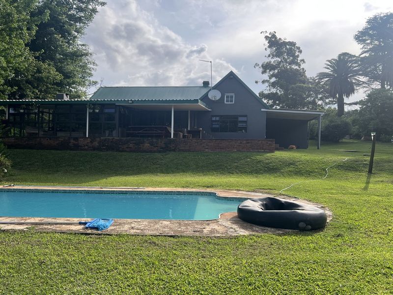 Rear view of the farmhouse featuring a swimming pool, expansive lawn, and a covered patio area with a metal roof.