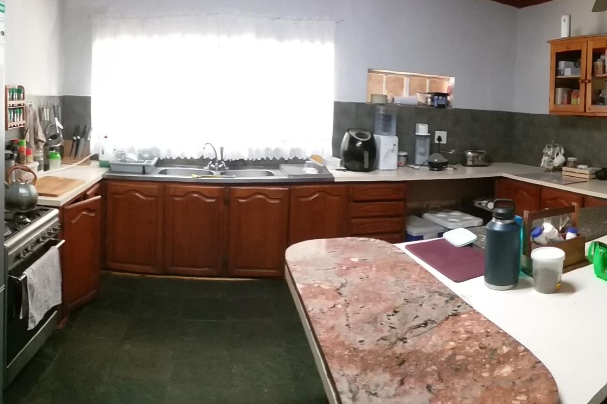 A functional kitchen featuring wooden cabinetry, a double basin sink, tiled splashbacks, and a spacious breakfast bar area.