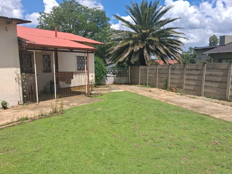 Rear garden area featuring a lawn, concrete patio, and precast concrete boundary wall with a metal security gate.