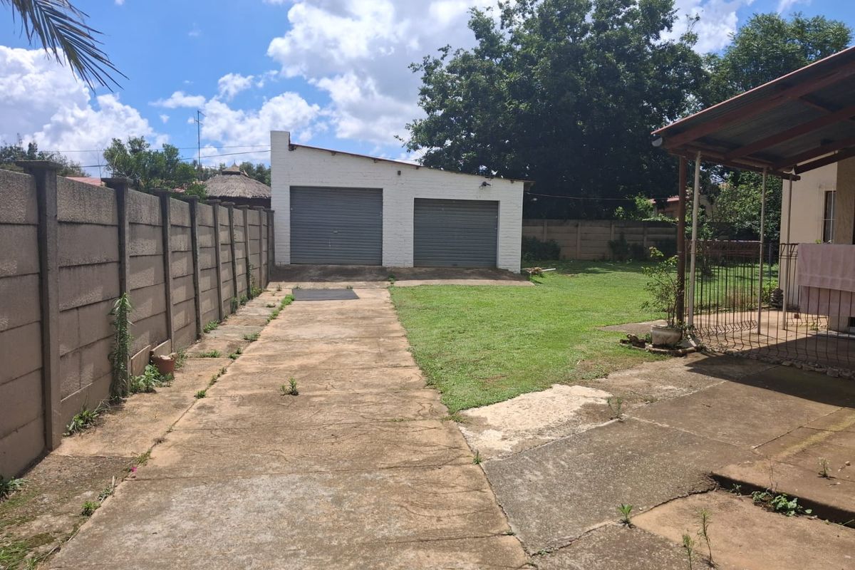 Rear garden area featuring a double garage, concrete driveway, and a covered patio space with a precast concrete boundary wall.