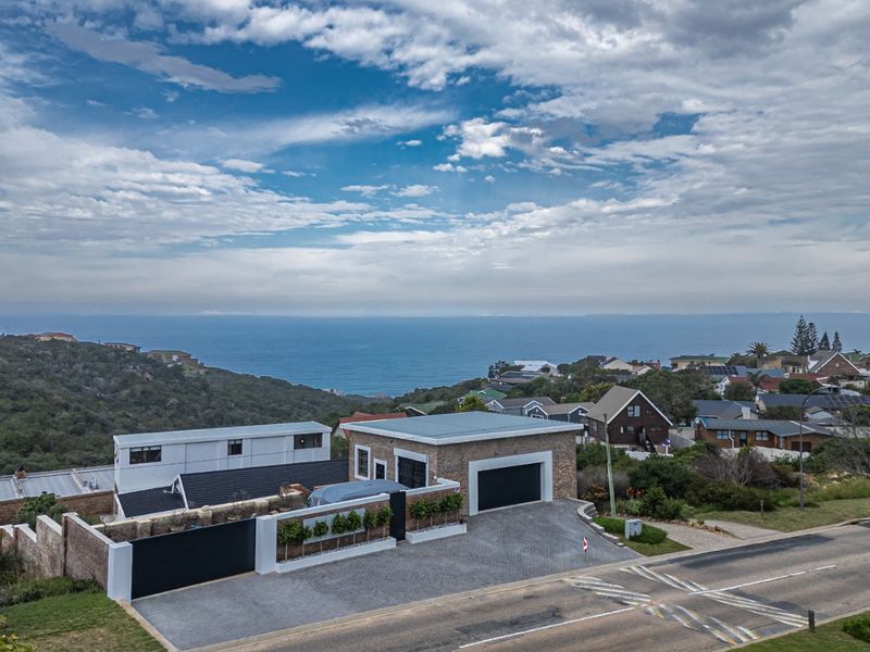 Aerial view of a modern residential property featuring a paved driveway, double garage, and brick exterior, set against a coastal landscape.