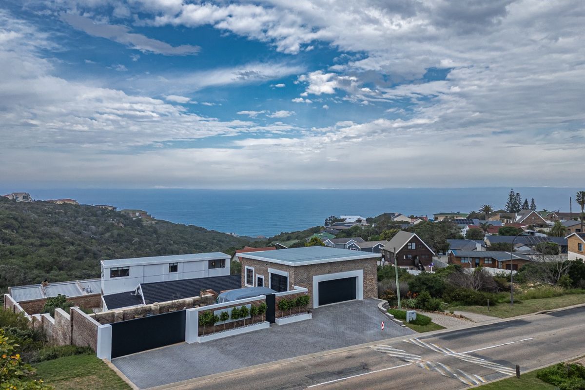 Aerial view of a modern residential property featuring a paved driveway, double garage, and brick exterior, set against a coastal landscape.