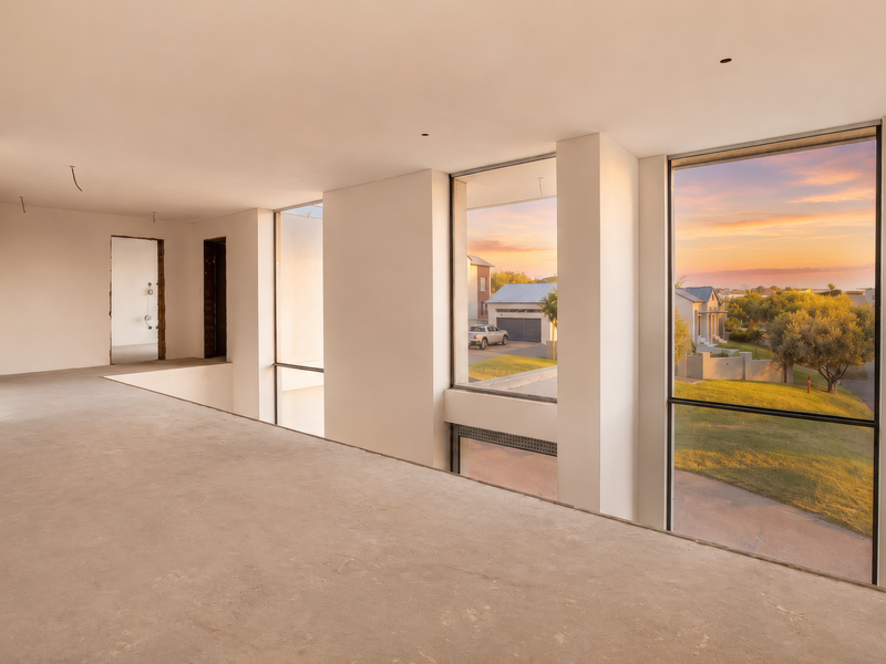 An expansive, unfinished interior space featuring large floor-to-ceiling windows with scenic views, ready for final flooring and interior finishes.
