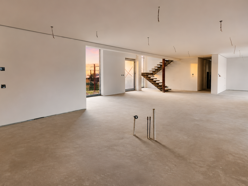 Spacious open-plan interior in shell condition, featuring a modern staircase, large sliding glass doors, and exposed utility connections ready for final finishes.