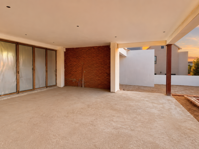 An unfinished covered patio area featuring exposed brickwork, concrete flooring, and large sliding glass doors, offering potential for a custom outdoor entertainment space.