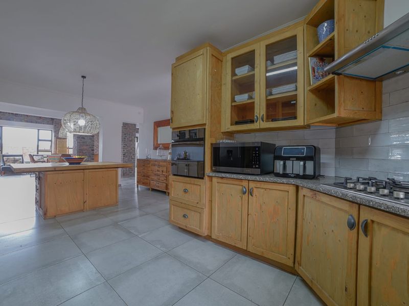 Open-plan kitchen featuring natural wood cabinetry, stone countertops, built-in oven, gas hob, and tiled flooring, flowing into the adjacent living area.