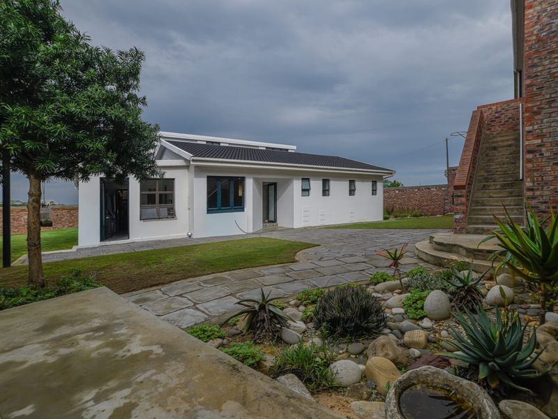 A view of the rear exterior featuring a white-painted building, stone-paved pathways, landscaped garden beds, and an external brick staircase.
