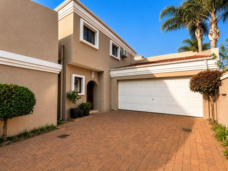 A well-maintained townhouse exterior featuring a paved driveway, double garage, and clean stucco facade with modern architectural detailing.