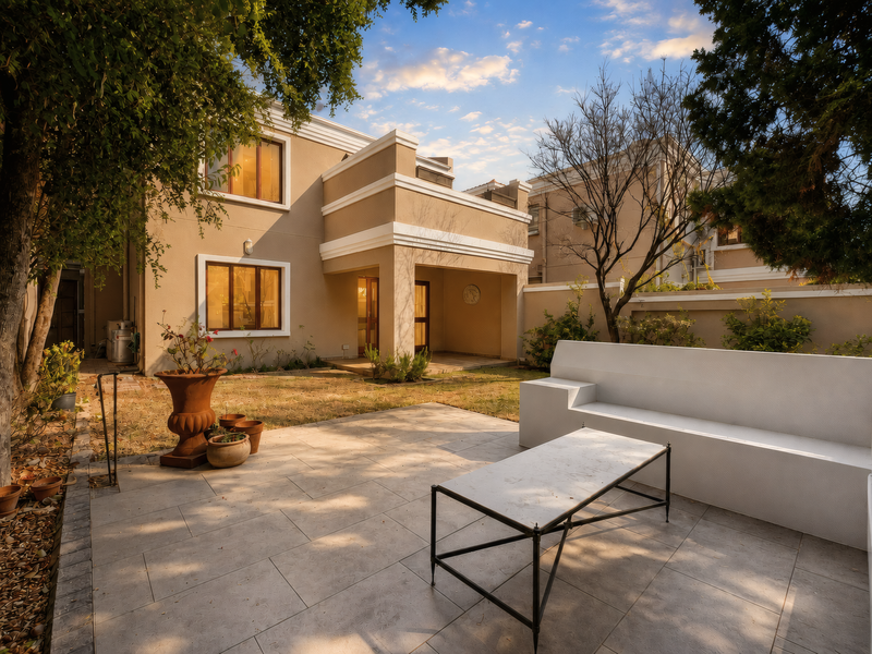 Rear view of the townhouse featuring a paved patio area, covered terrace, and private garden space with boundary walls.