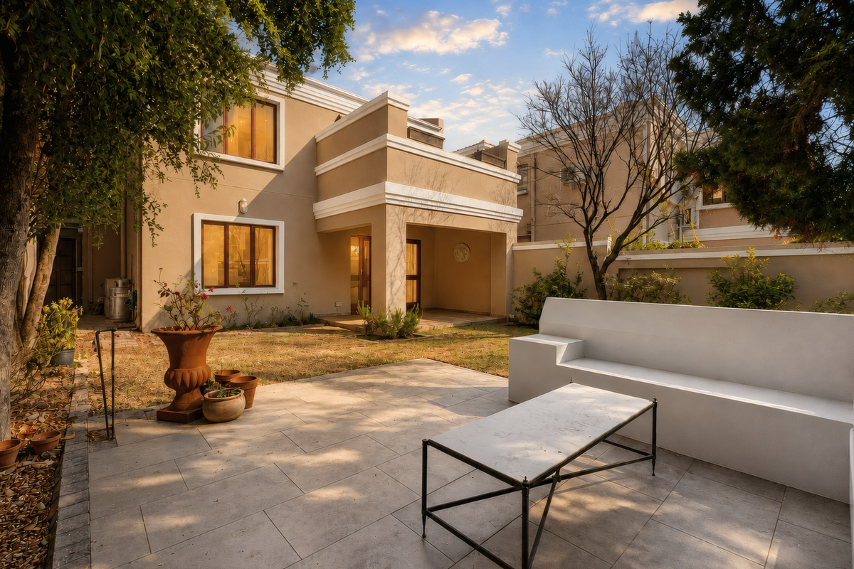 Rear view of the townhouse featuring a paved patio area, covered terrace, and private garden space with boundary walls.