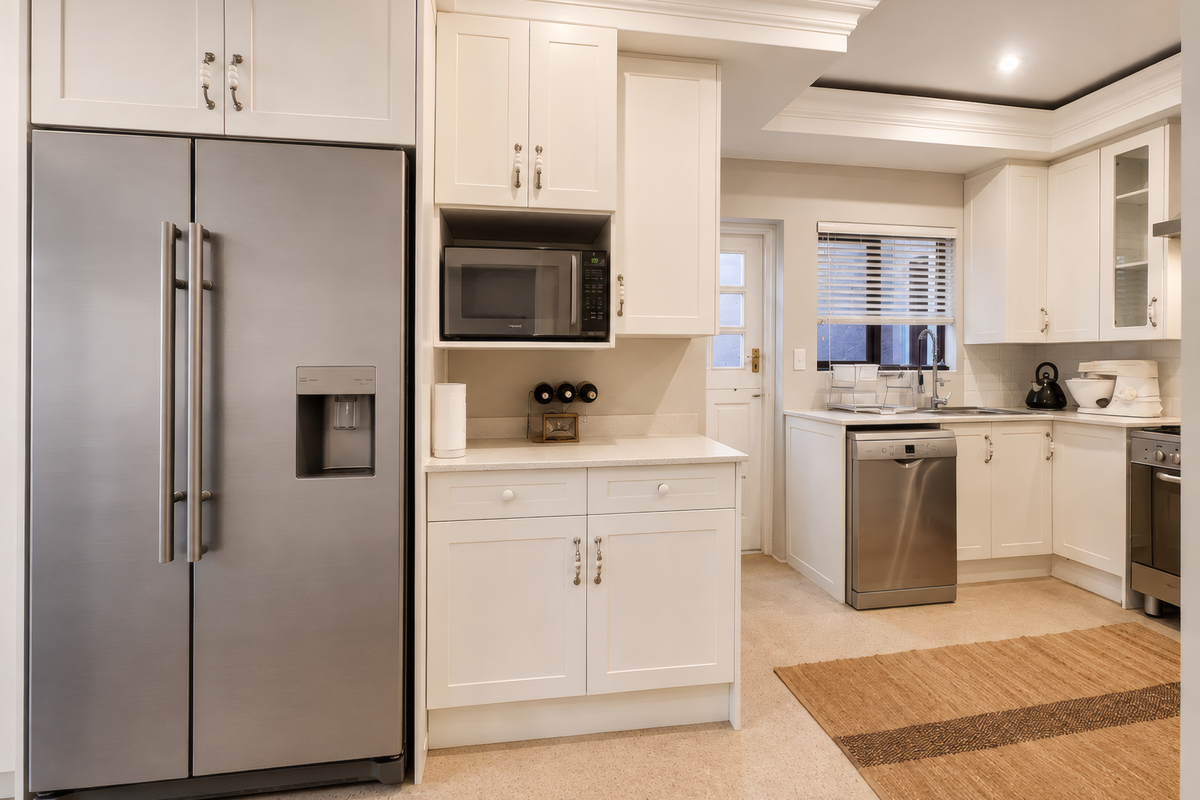 A well-maintained kitchen featuring white cabinetry, stone countertops, integrated appliances, and a tiled backsplash, offering a clean and functional culinary space.