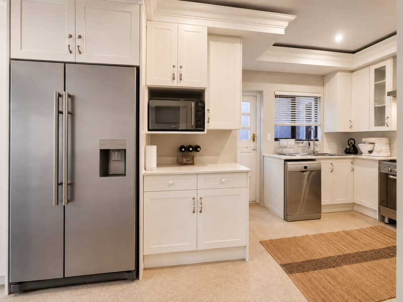 A well-maintained kitchen featuring white cabinetry, stone countertops, integrated appliances, and a tiled backsplash, offering a clean and functional culinary space.