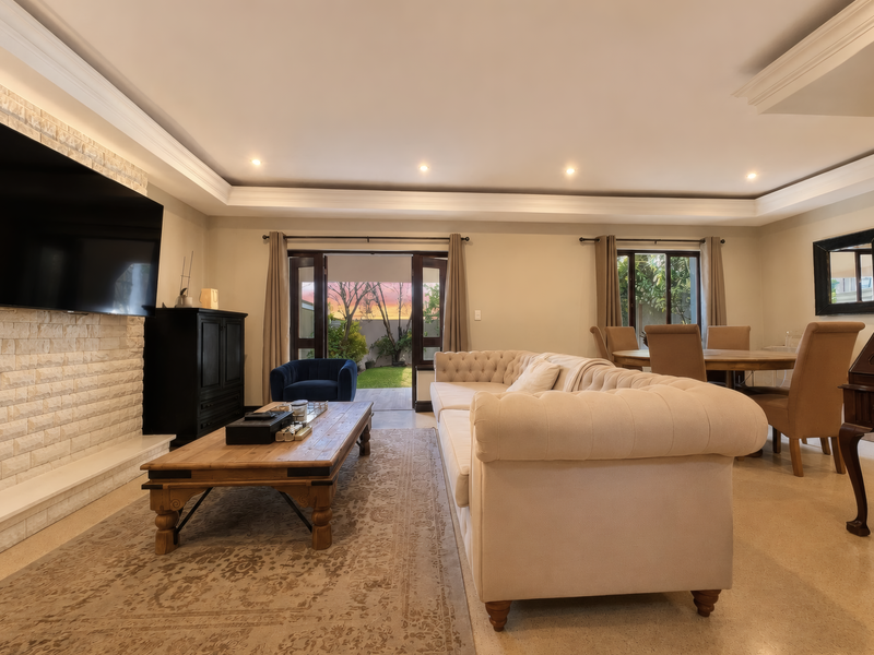 Spacious open-plan living and dining area featuring stone fireplace cladding, elegant crown molding, recessed lighting, and direct access to the rear garden through french doors.
