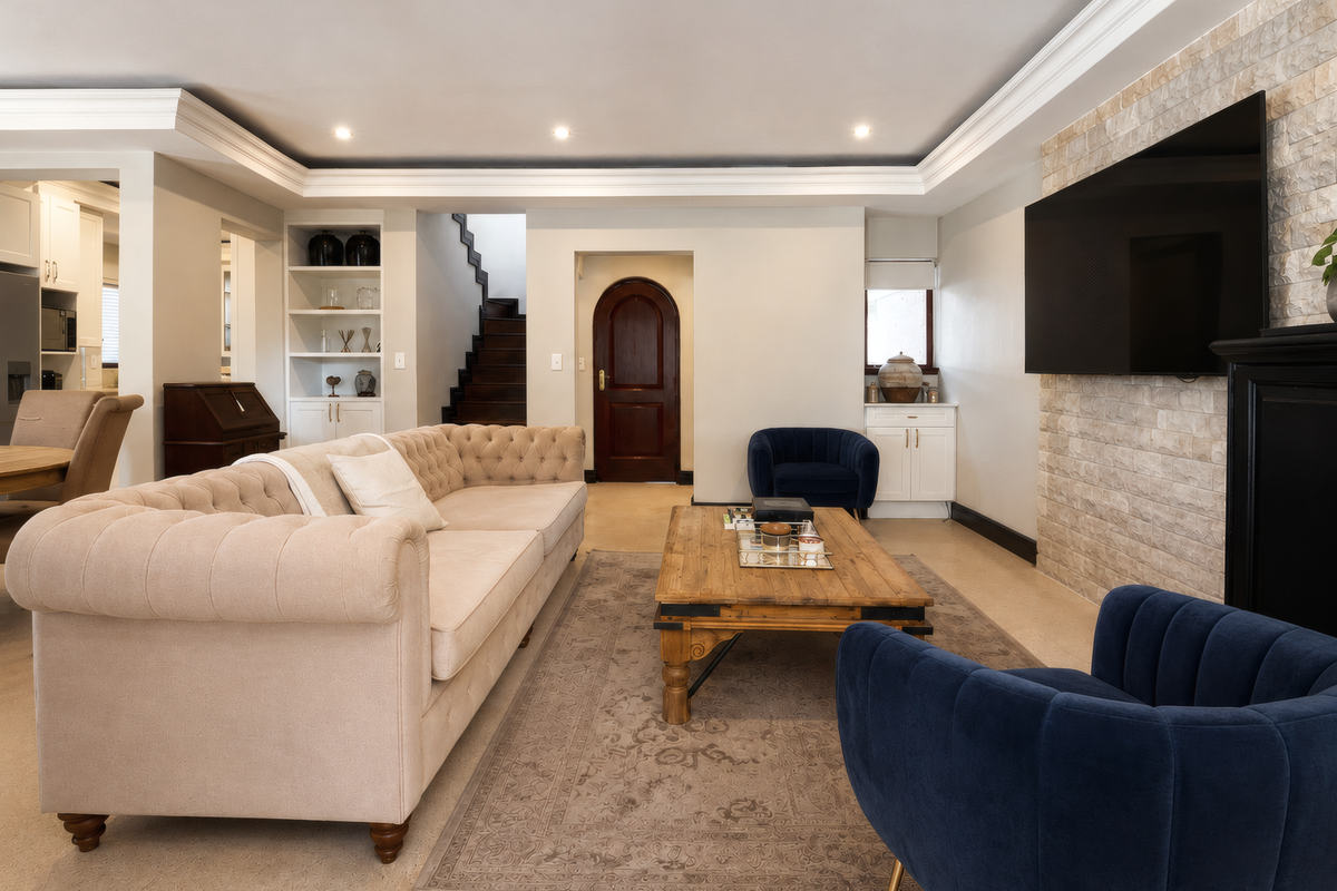 Spacious living room featuring a stone accent wall, built-in shelving, crown molding, and elegant architectural details including an arched doorway and staircase.