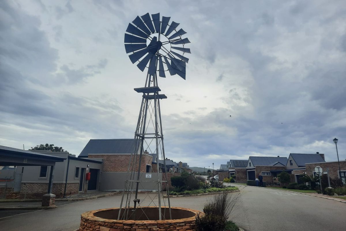 A view of the residential estate entrance featuring a decorative windmill and stone-clad base, set against a paved driveway and surrounding residential properties.