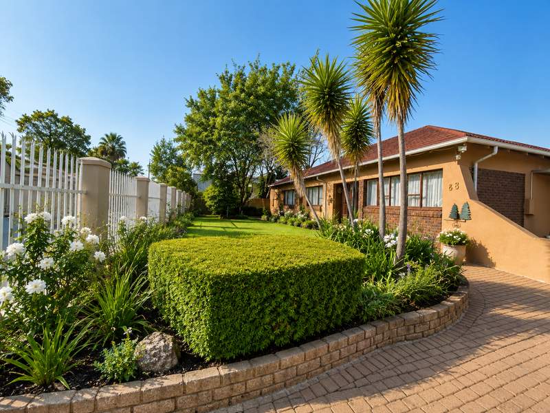 A well-maintained front exterior featuring a brick facade, paved driveway, and a neatly landscaped garden with established trees and security fencing.