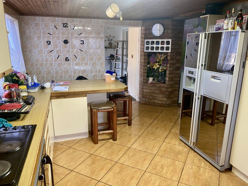 A functional kitchen featuring a timber breakfast bar, brick feature wall, tiled splashback, and tiled flooring with a timber-paneled ceiling.