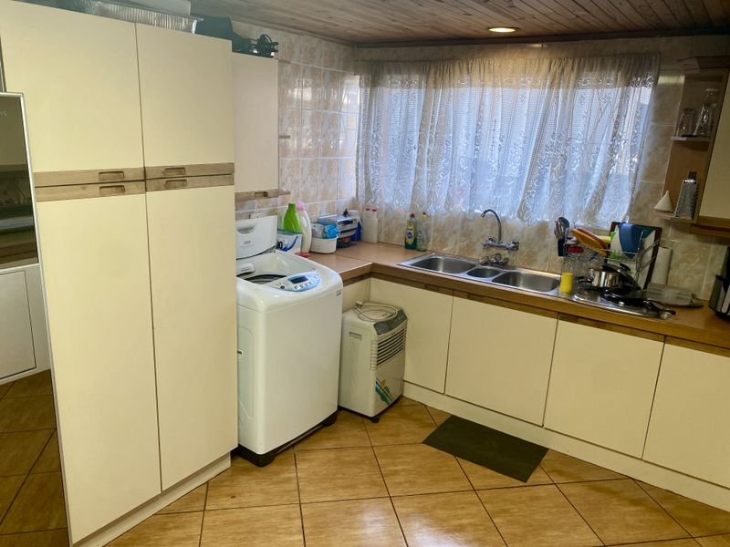 A functional scullery area featuring built-in cabinetry, a double basin sink, tiled splashbacks, and timber ceiling finishes.