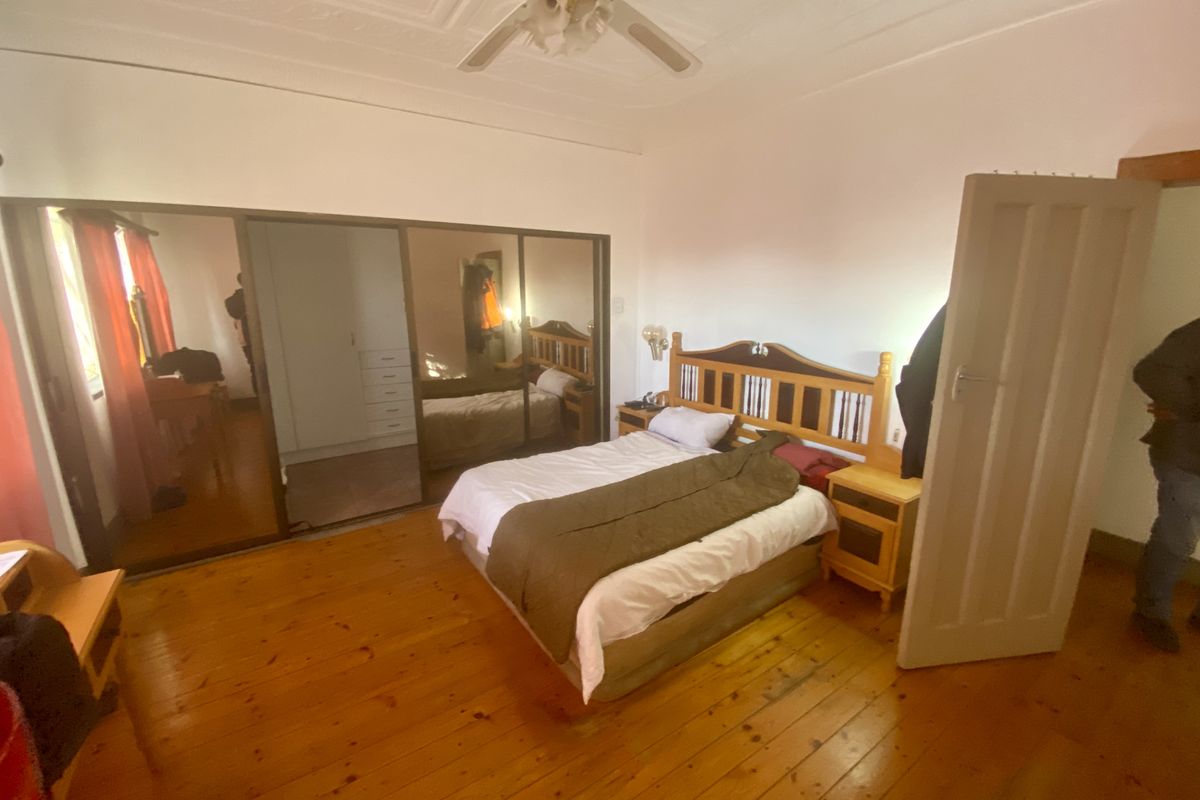 A bedroom featuring polished timber flooring, a built-in mirrored wardrobe, and a decorative pressed metal ceiling with a central fan.