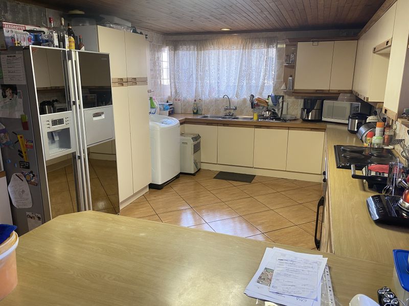 A functional kitchen featuring laminate countertops, built-in cabinetry, a double sink, and an electric hob, finished with tiled flooring and a timber ceiling.