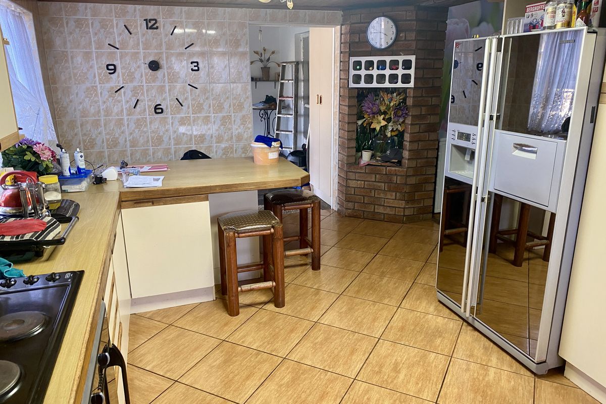 A functional kitchen featuring a brick accent wall, timber ceiling, and tiled flooring, offering a dated aesthetic with potential for modern renovation.