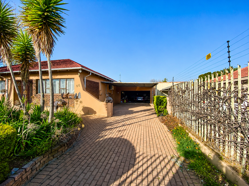 Front exterior view of the property featuring a paved driveway, carport, and secure boundary wall with electric fencing.