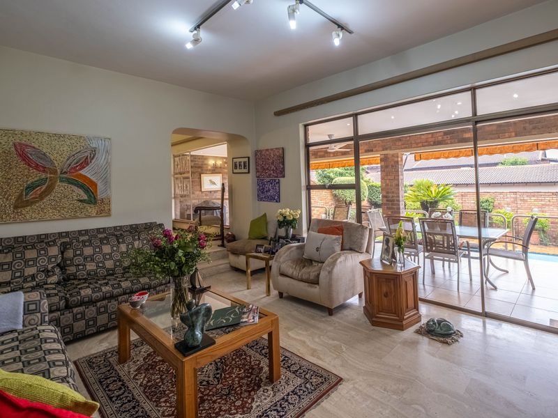 Spacious living room featuring elegant travertine flooring, track lighting, and large sliding glass doors that provide seamless access to the outdoor patio area.