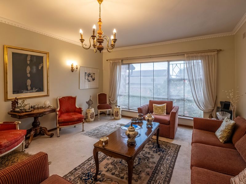 A traditional living room featuring crown molding, a central chandelier, and a large window providing natural light.