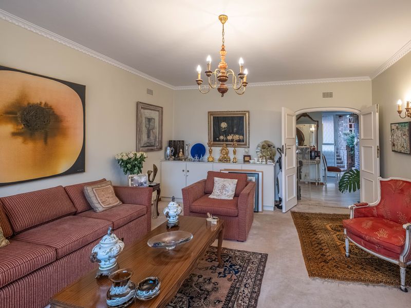 A traditional living room featuring crown molding, built-in cabinetry, and double doors leading to an adjacent space, illuminated by a central chandelier and wall sconces.